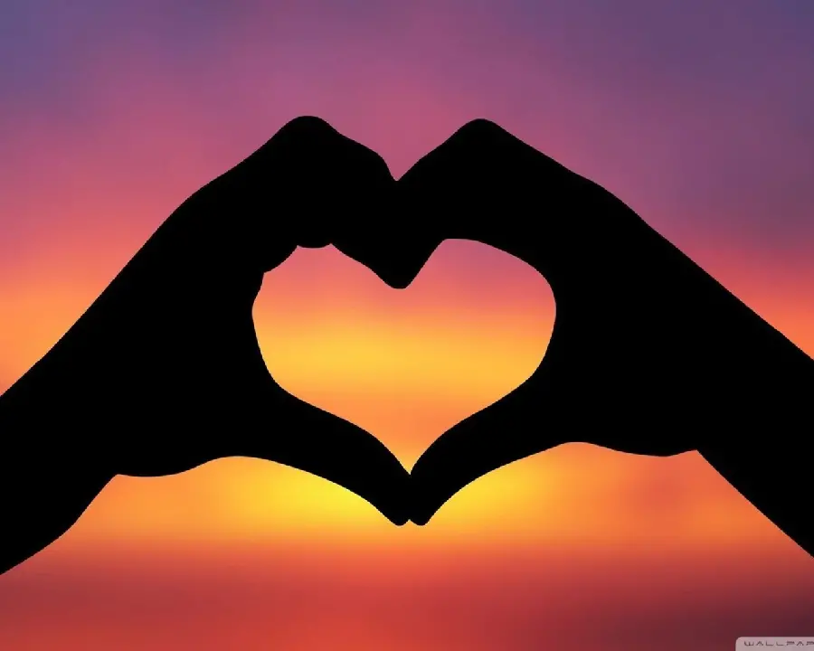 Photo of a heart made with the hands of two lovers at sunset
