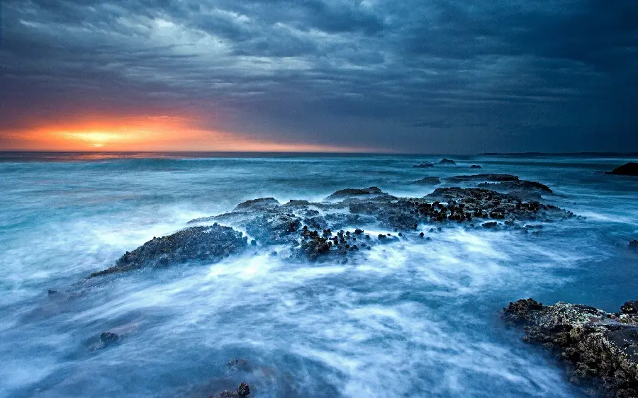 Photo of Blue Ocean Waves Crashing on the Rocks with the Penetrating and Interesting Sunlight at Sunset in Original Quality