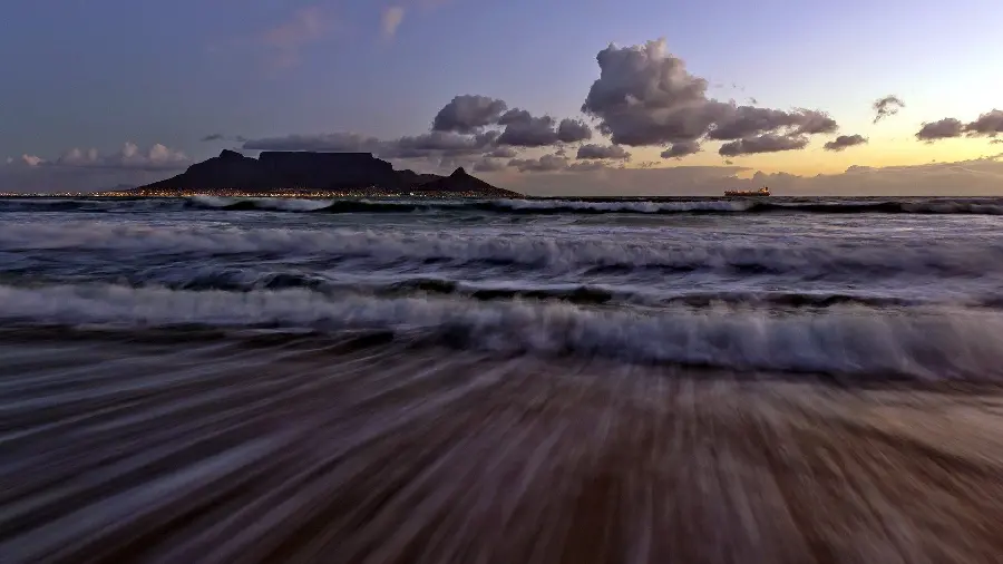 Attractive artistic photo of parallel movement of sea waves from close up under a cloudy and beautiful sunset sky and with a mountain and city background in excellent quality