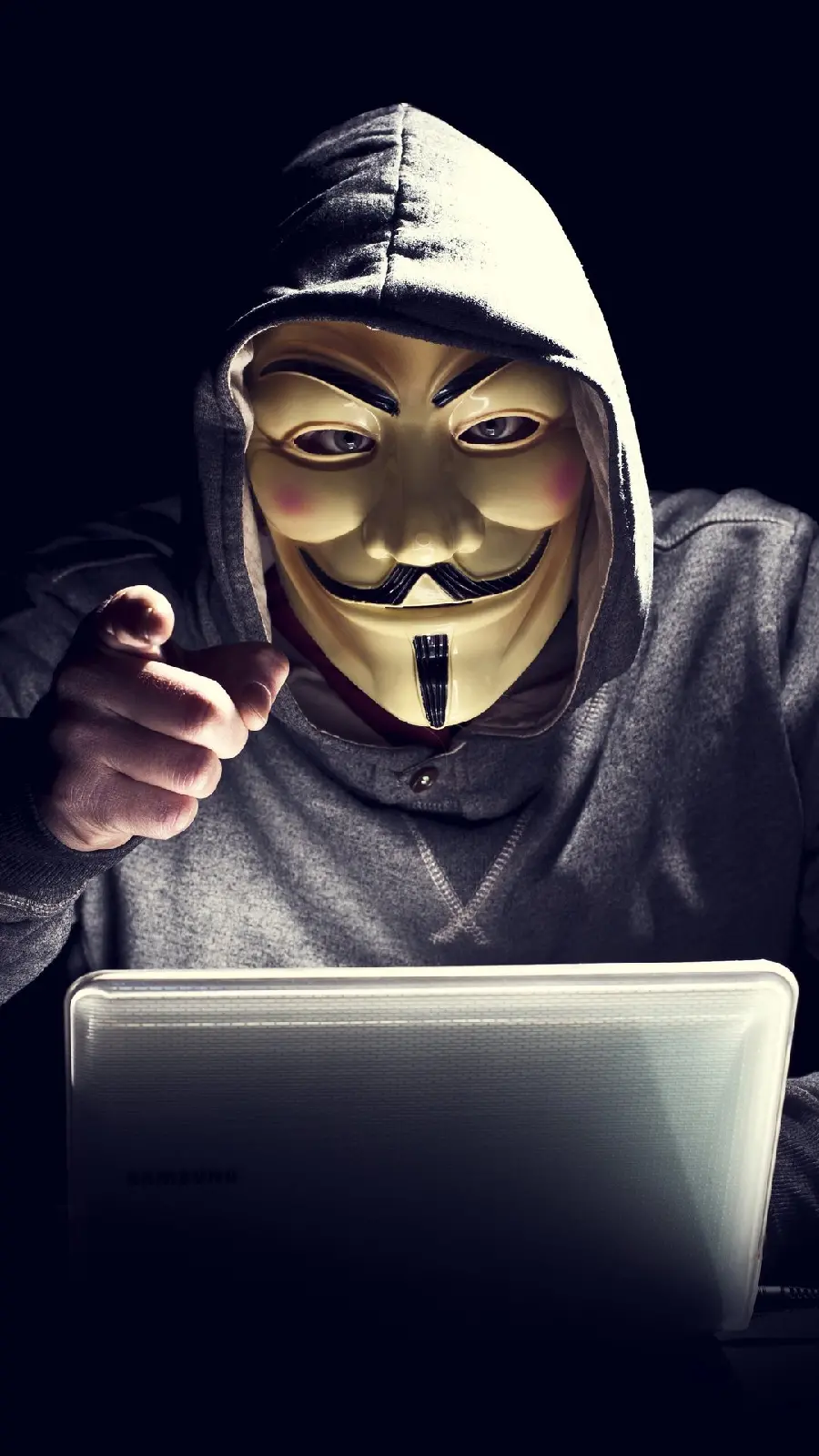 Photo of a hacker with a dolly mask behind a laptop hacking