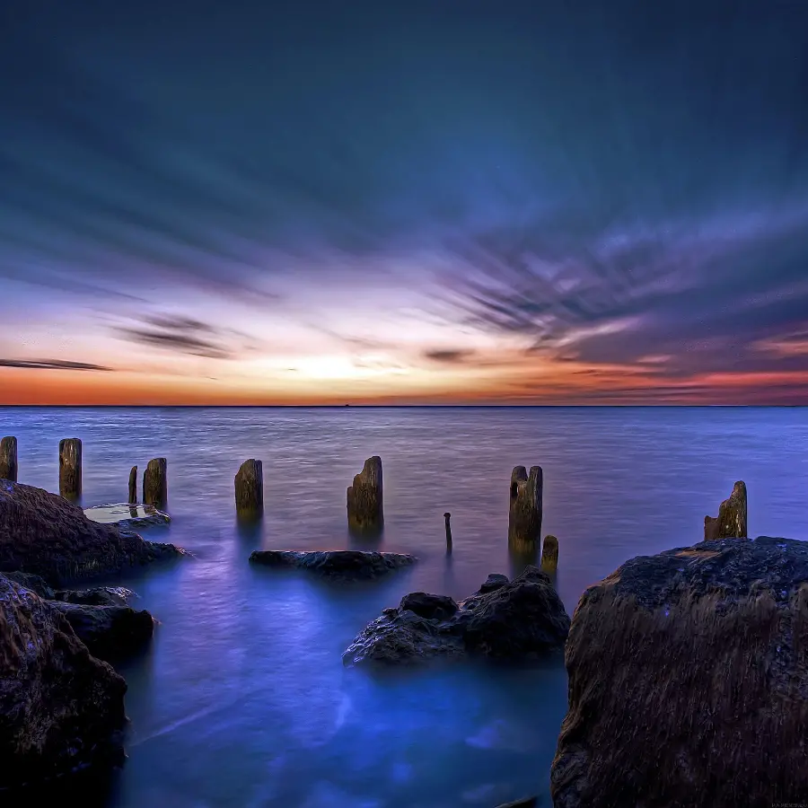 Impressive profile photo of the blue ocean at sunset with a blue and orange theme and with small cylindrical rocks with the best quality