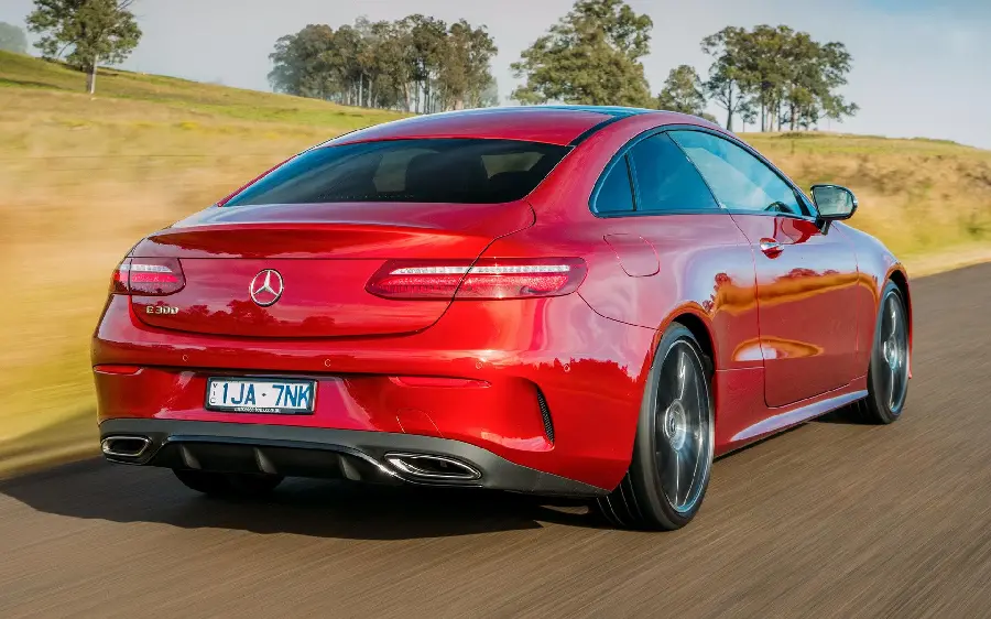 High quality background of the rear view of a red Mercedes-Benz E300 in a farm