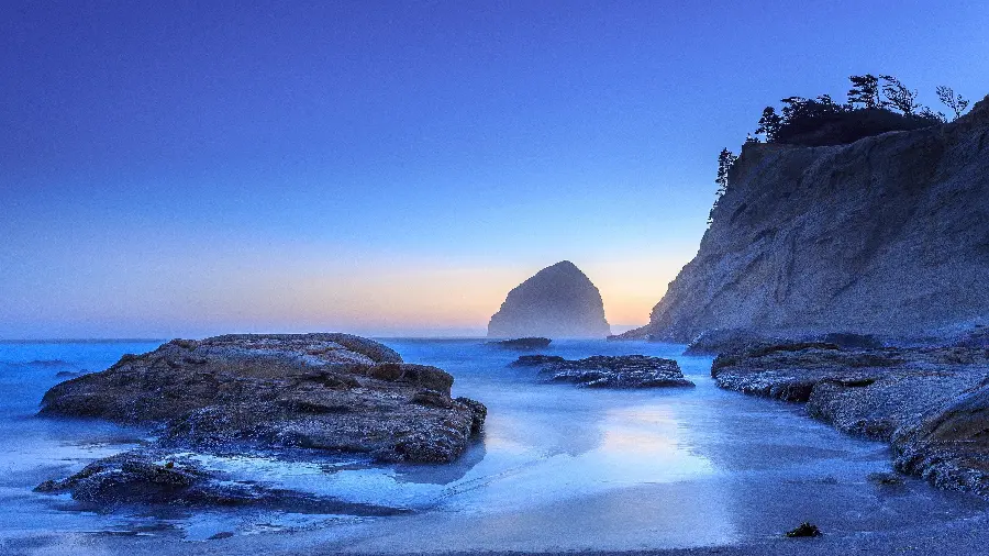A dreamy blue wallpaper of short and long rocks on the ocean shore in very high quality
