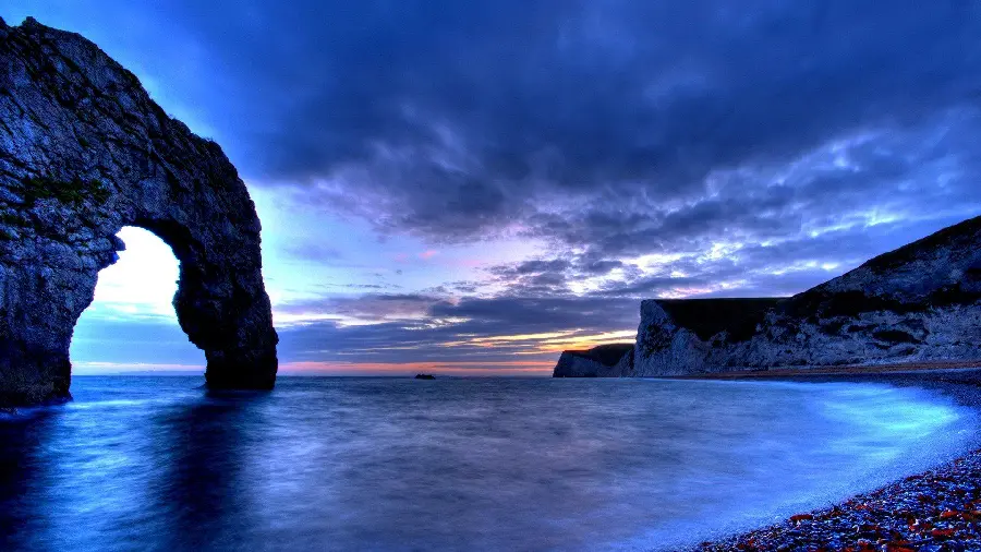 The most popular computer background with the image of the blue ocean in a dark space next to beautiful rocks in original quality