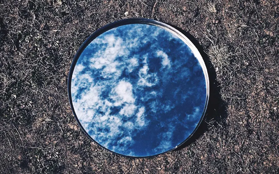 Creative wallpaper with the title of a mirror placed on the ground, in which the image of clouds and the blue sky is reflected
