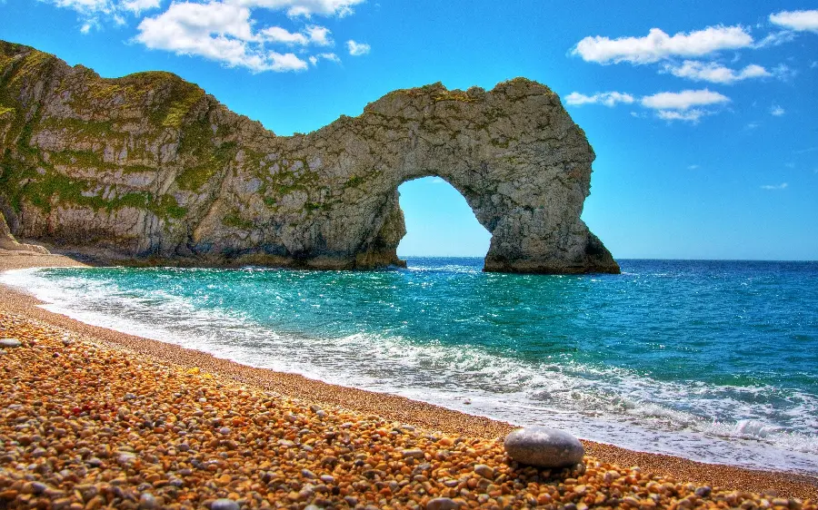 Download the image of a beautiful ocean beach next to an interesting rock on a sunny day