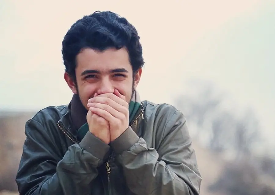 Ali Shadman smiling with a coat and scarf in cold weather, suitable for wallpaper