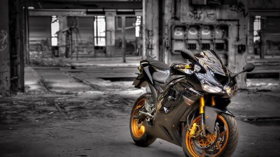 Download a background of a black motorcycle with a golden rim next to a ruined building