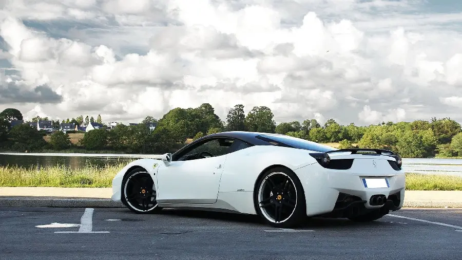 Download a picture of a white Ferrari from the left side next to a lush forest