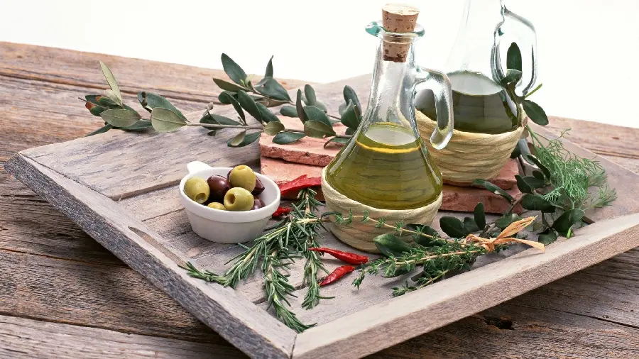 Attractive background of a bottle containing olive oil with a small container of olives and its fallen leaves around it