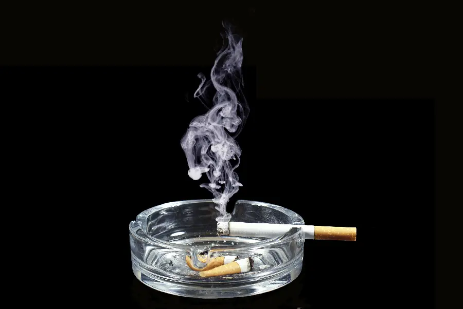 A special background image of a round glass ashtray with 2 extinguished cigarettes and lighted cigarette smoke next to it
