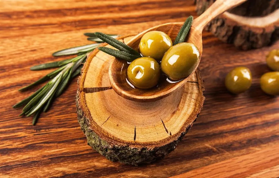 Download beautiful stock photo of three olives in a wooden spoon on a brown wooden stick