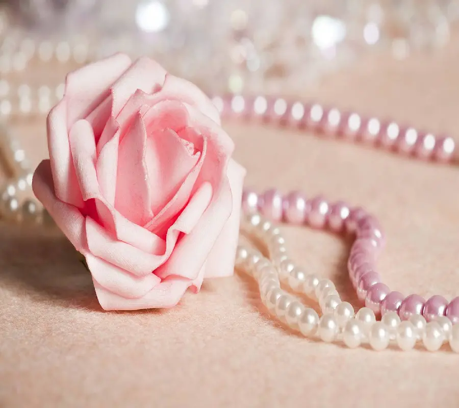 Background of two pearl necklaces in white and pink next to a pink flower
