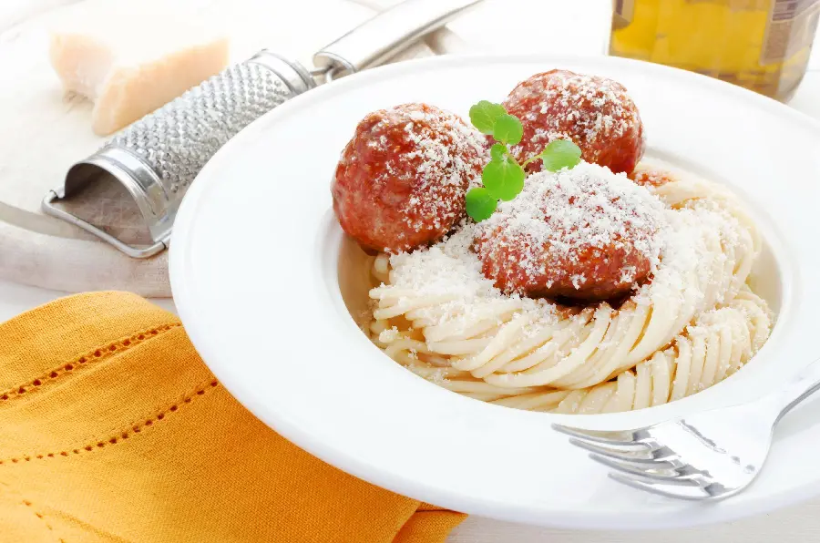 Full HD quality background of meatballs with pasta with red sauce and grated cheese and a small green plant on a white plate