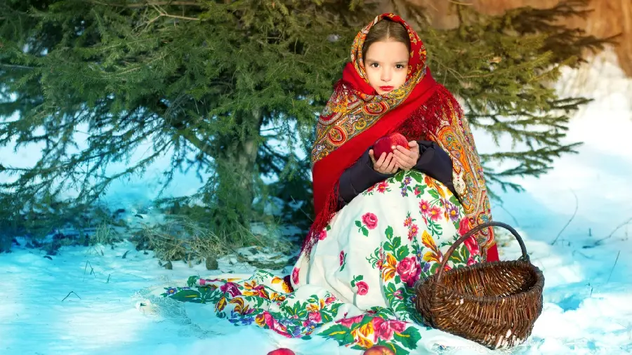 A striking stock photo of a cute and kind little girl with a red apple in her hands with a basket next to her and a green tree