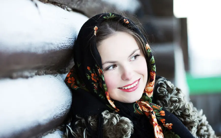 Download attractive photo of a beautiful Russian girl with a black floral scarf leaning on a wooden hut in HD quality suitable for mobile