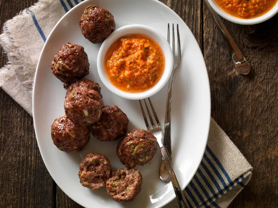 Beautiful high-quality photo of a delicious and interesting meatball with sauce in an oval dish with two forks next to it