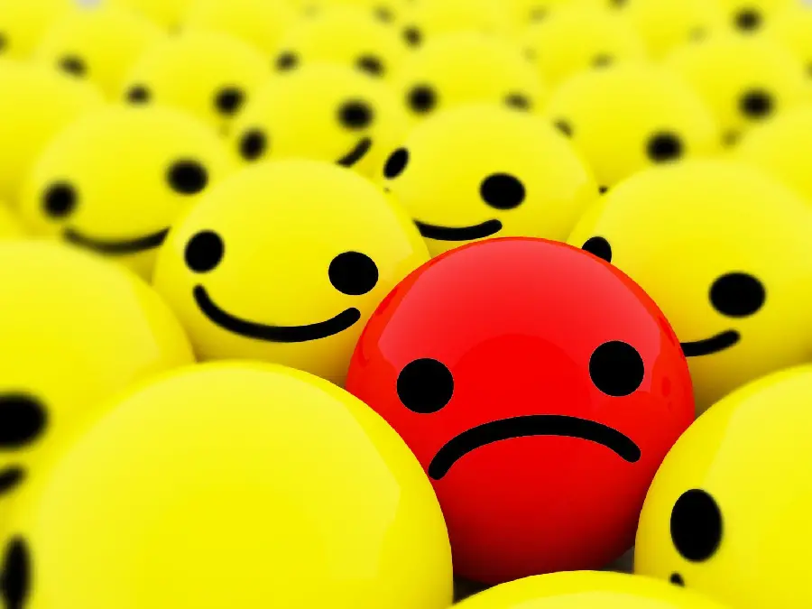 Image of a sad red emoji among several happy emojis