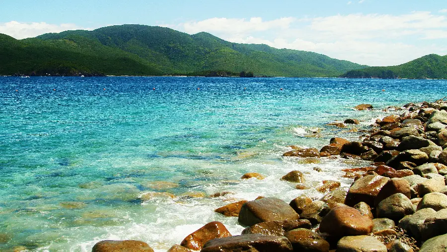 A special laptop background of the refreshing ocean and green mountains and small and large rocks next to it