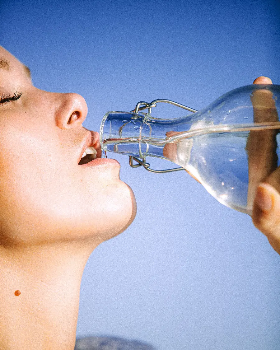 Photo of a woman in Drinking clear water from a high-quality glass bottle suitable for tablets