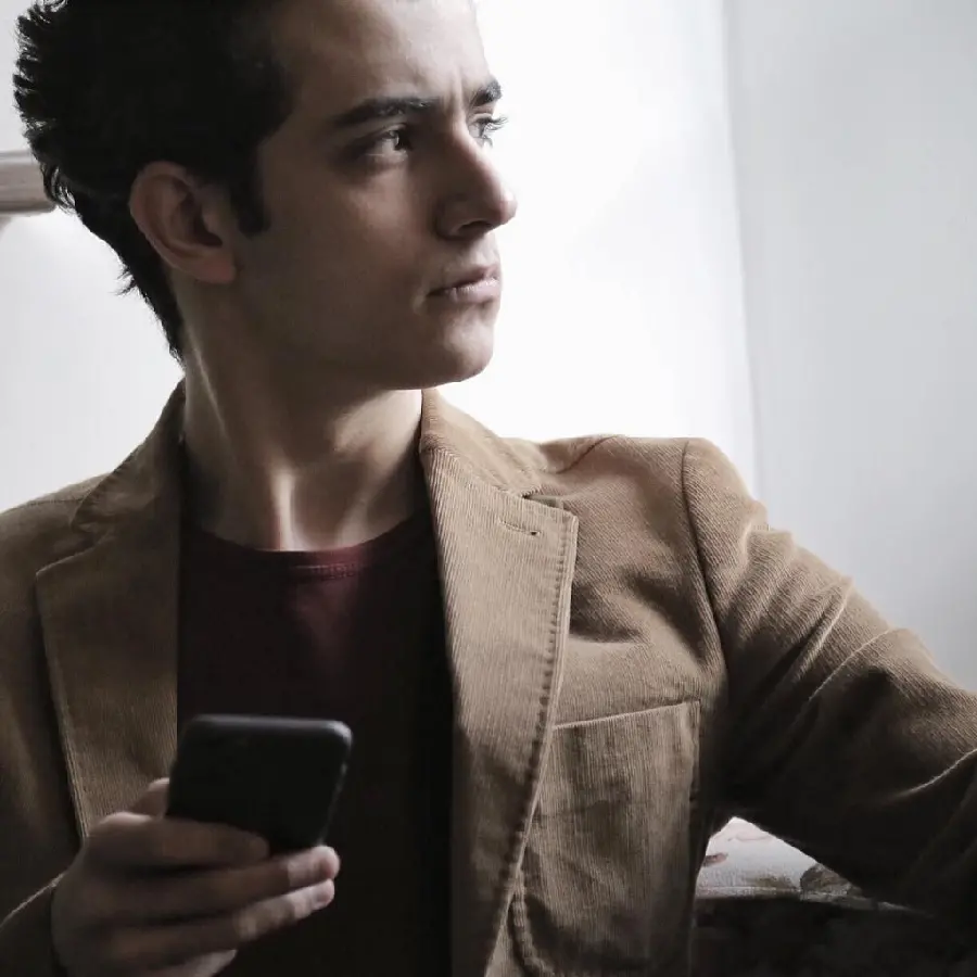 A photo of Ali Shadman as a teenager with a brown coat and a mobile phone in his hand