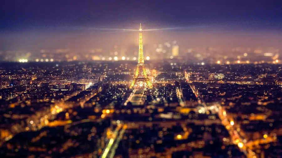 Download a blurry image and a distant view of the Eiffel Tower in the city of Paris, cultural center at night