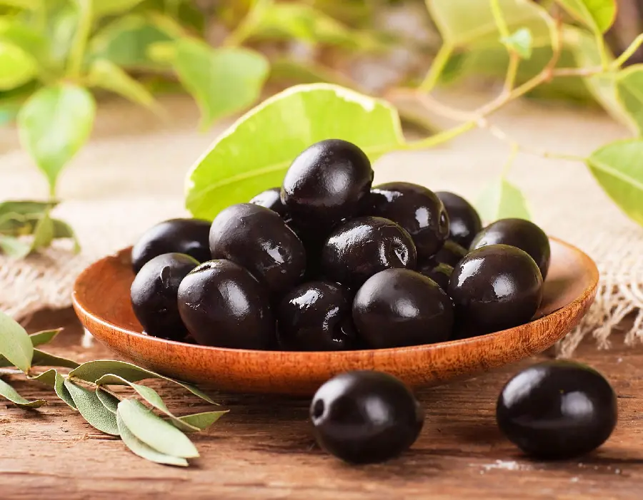The most visited background of a brown plate with black olives and two fallen numbers next to it with green leaves around it