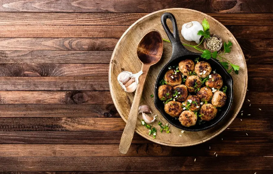 The most important stock image of a common and delicious meatball dish roasted in a frying pan with garlic and a sprig of parsley on a wooden table