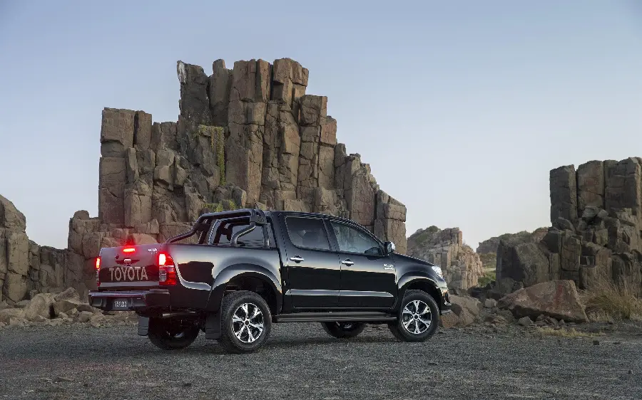 Full Quality Stock Image of Shiny Black Toyota Hilux Next to Rocky Cliffs