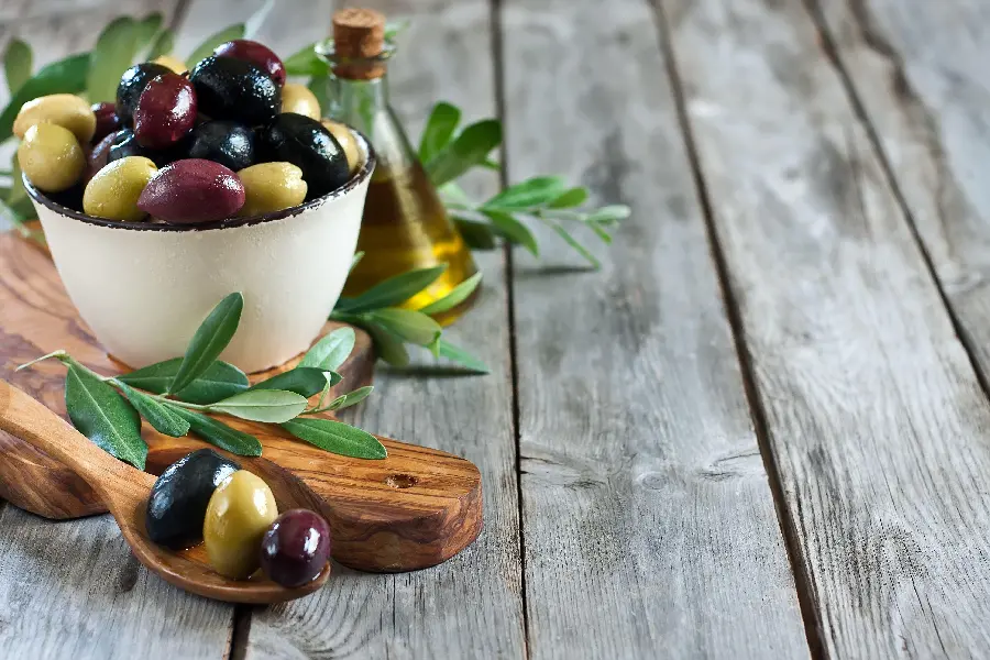 Exceptional image of a white bowl full of olives with a beautiful glass of wine Grinder and board and wooden spoon