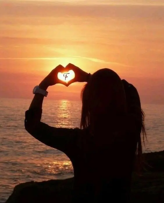 Download beautiful background of a girl by the sunset beach holding a heart with the letter F Done