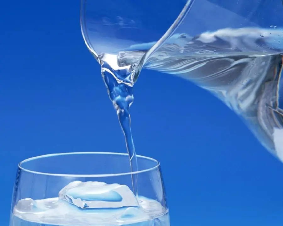 Blue background of the moment of pouring drinking water from a pitcher into a glass