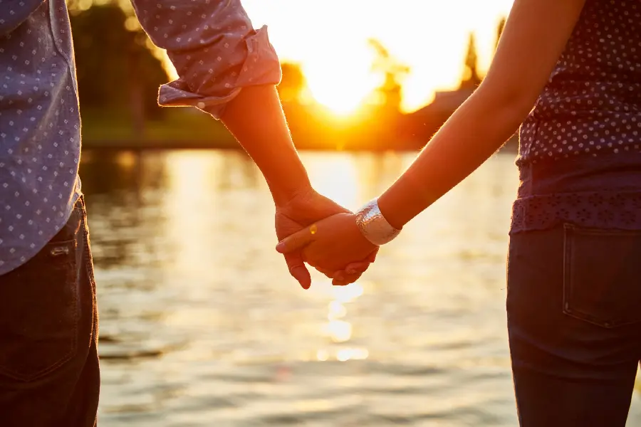 Romantic photo of two people holding hands at sunset