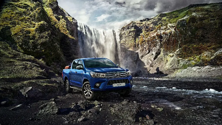A modern high-quality natural background photo of a light blue Toyota Hilux in the mountains and next to a waterfall for your tablet