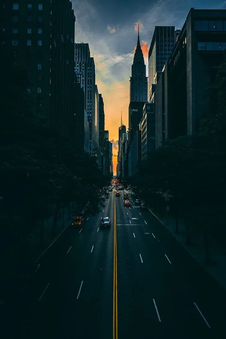 A dark and orderly poster of skyscrapers on both sides of the street and cars moving on a city road