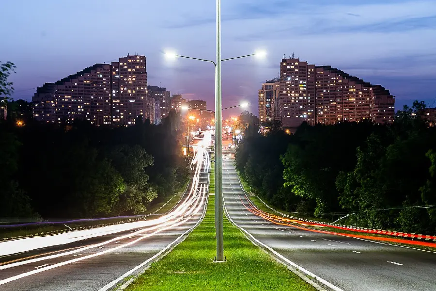 Download a magical and beautiful and illuminated profile photo of green space and lights between a city road and buildings at the bottom
