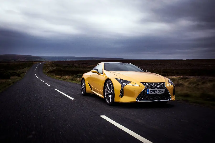 Stock image of a bright yellow Lexus LC 500 on a street with a dark cloudy sky