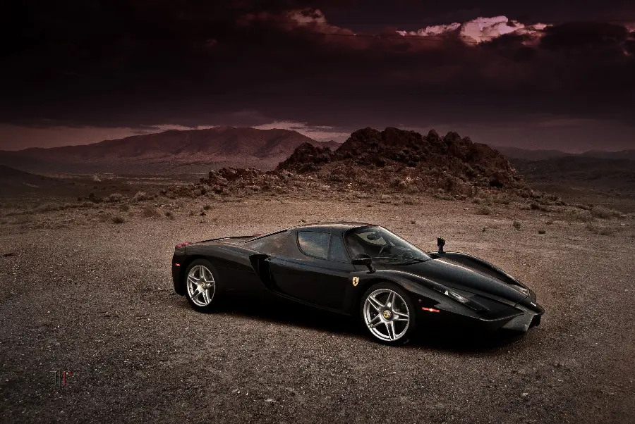 Background photo of a small and sporty black Ferrari Enzo on a dirt road