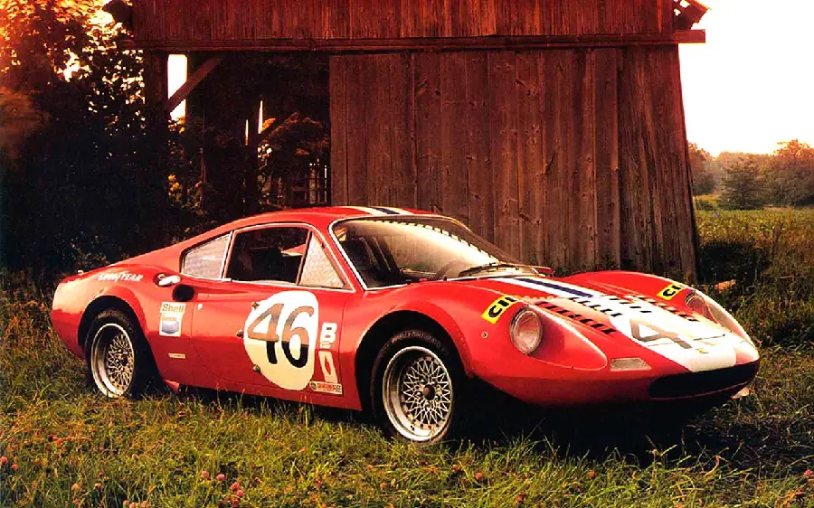 Download an attractive wallpaper of an old and classic Ferrari car next to a wooden hut and a meadow High quality