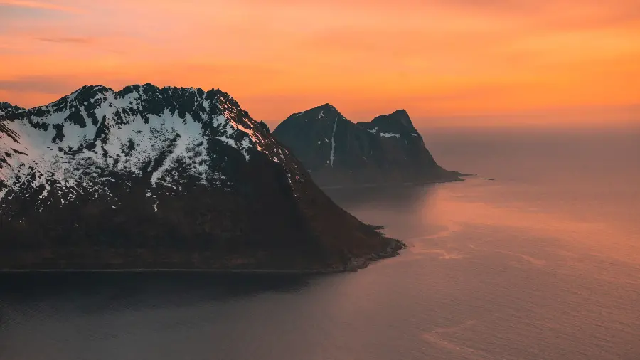 Download the background of the orange sunset of the ocean and the peaks of the mountains covered with snow