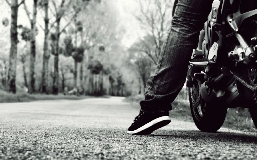 Fresh black and white background photo of a black motorcycle rider's leg on a forest road