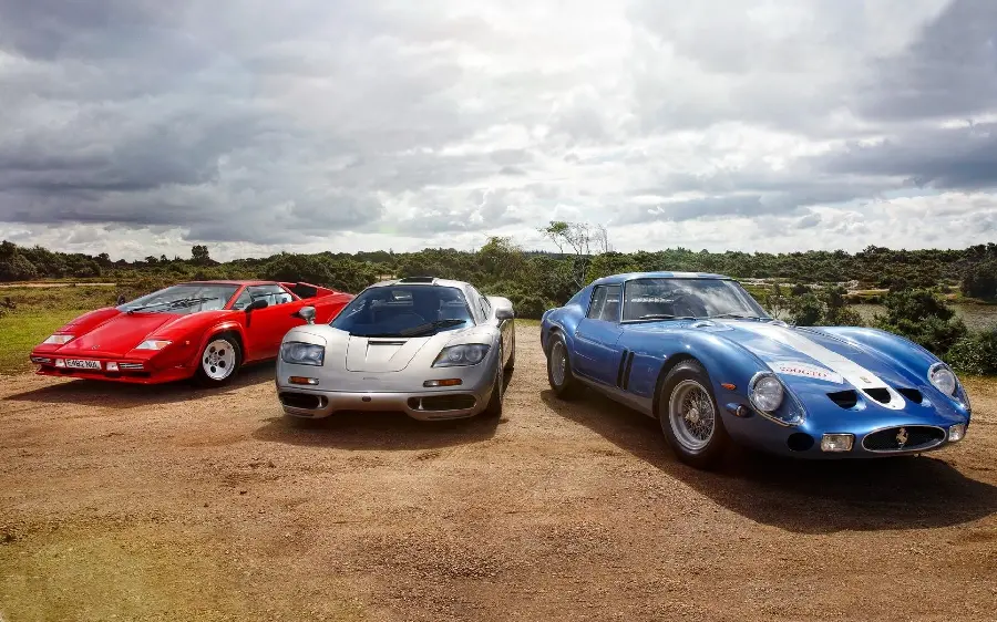 Beautiful stock photo of 3 old and classic Ferrari cars in blue, silver and red colors with a cloudy sky