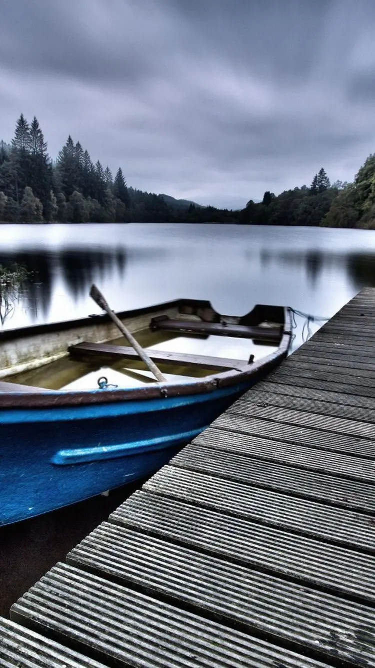 Photo of a lonely wooden boat by the lake under cloudy weather for the phone background