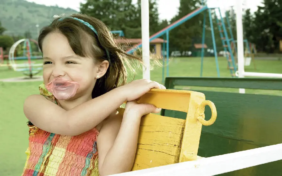 Funny and funny picture of a little girl in the park with gum stuck to her face