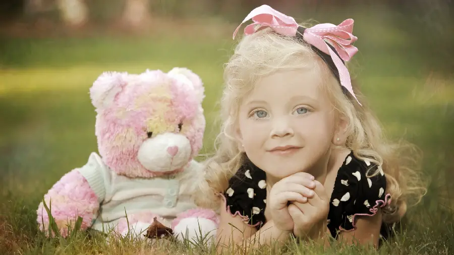 Photo of a little girl with blonde hair next to a teddy bear