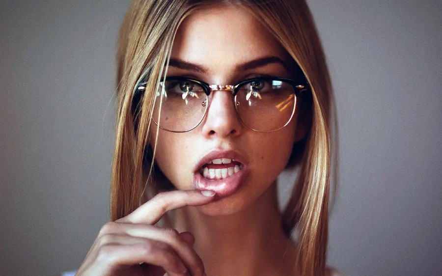 Beautiful girl with glasses and golden hair with a seductive finger-to-mouth gesture