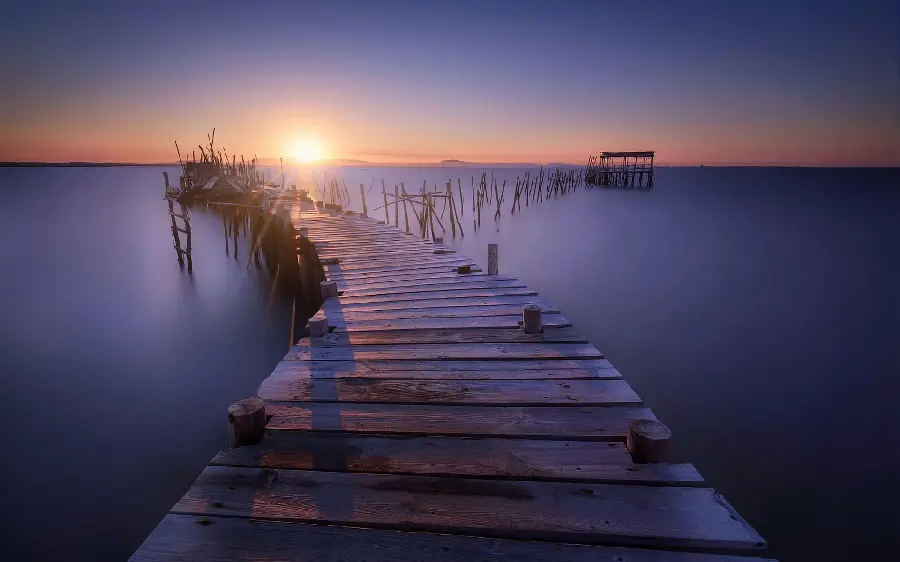 A beautiful picture of a sunset on the sea and a wooden bridge