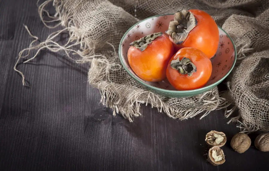 A charming background photo of orange persimmons in a turquoise bowl