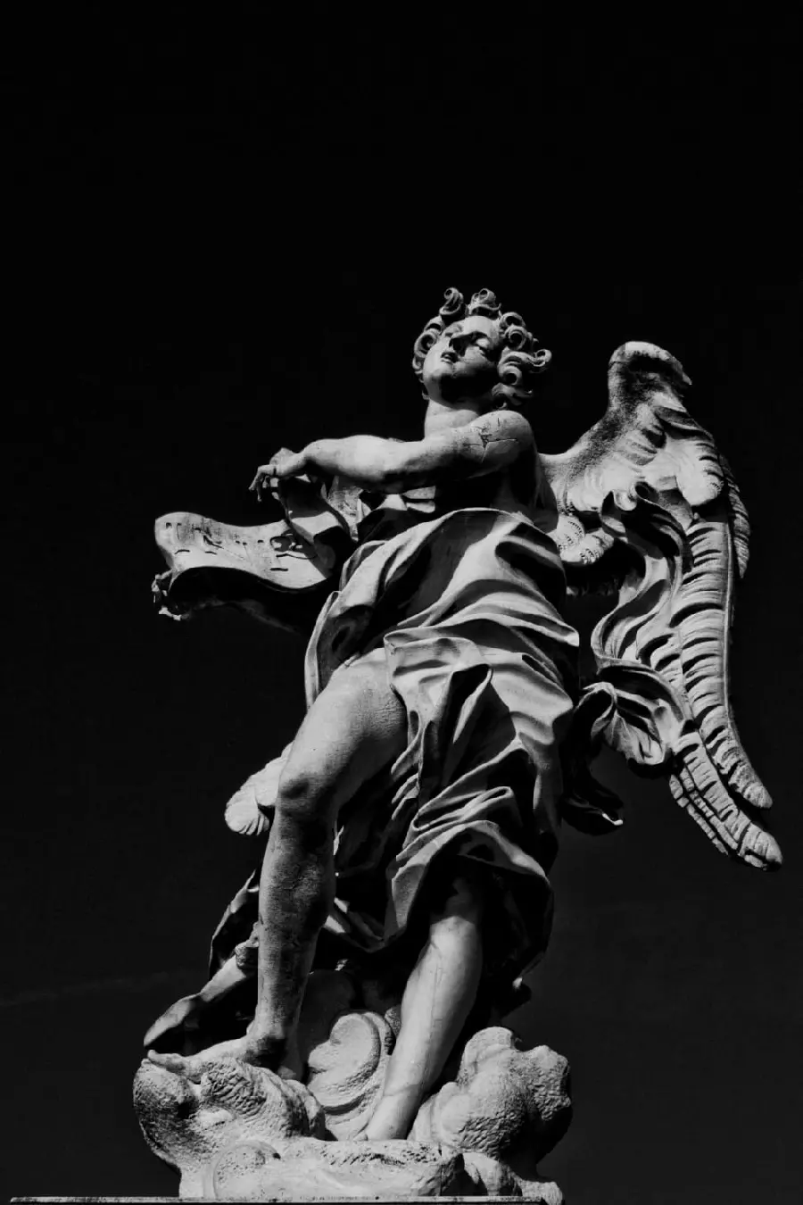 Dark photo of a winged stone angel statue with a black background