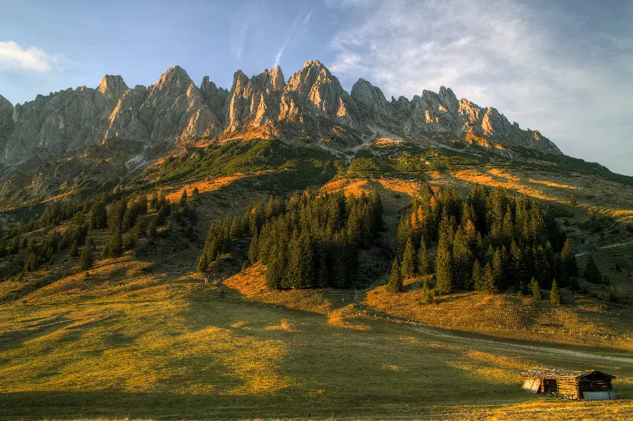 Download a sunny photo of a mountain with a lively and green slope and a small hut next to it